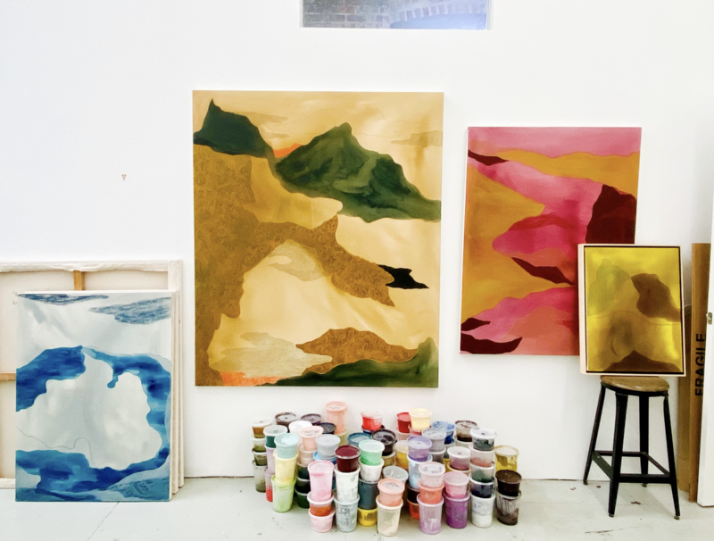 A studio view of artist Mel Reese with tubs of paint stacked in front. 